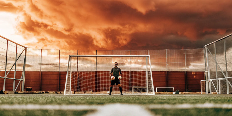 Soccer goalkeeper with essential training equipment and soccer balls in front of a goal.